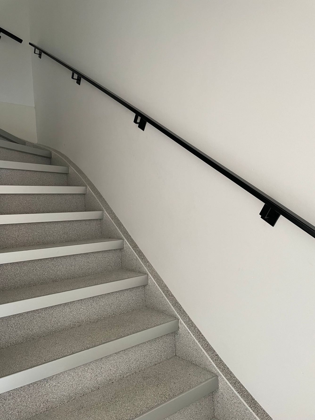 Stalen trapleuning die met de trap meeloopt langs een witte wand